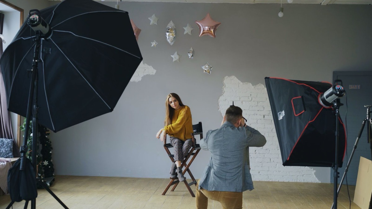 A photographer taking a portrait of a seated subject in a lit studio